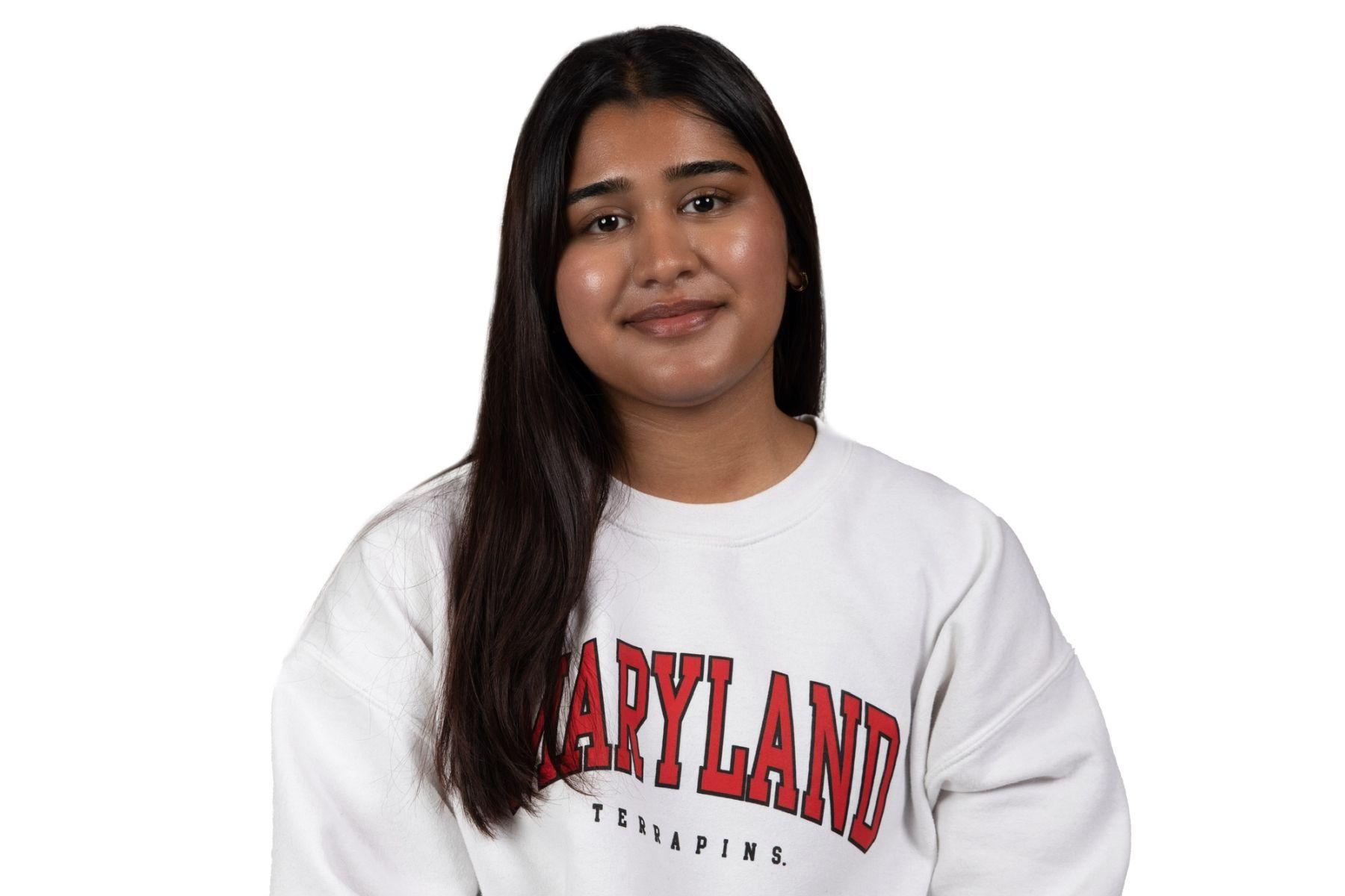 Preethi is wearing a white Maryland sweatshirt and is smiling at the camera