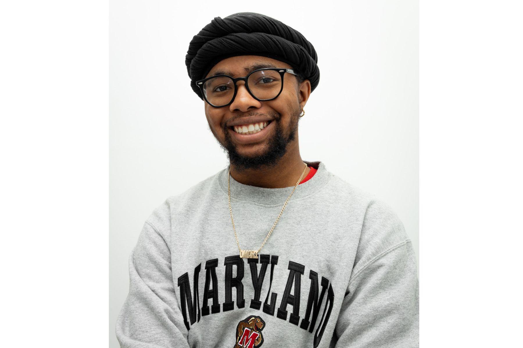 Omari is wearing a gray Maryland sweatshirt and is smiling at the camera