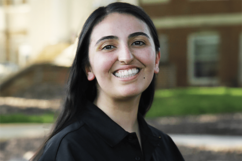 Ashley is pictured wearing a black orientation polo shirt and smiling at the camera