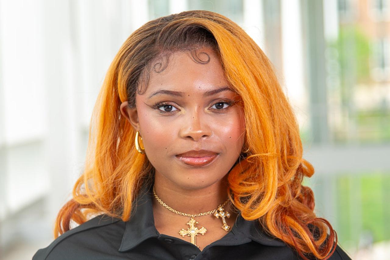 TA Hadassah with curled reddish blonde (orange) hair with gold hoop earrings and gold cross necklace