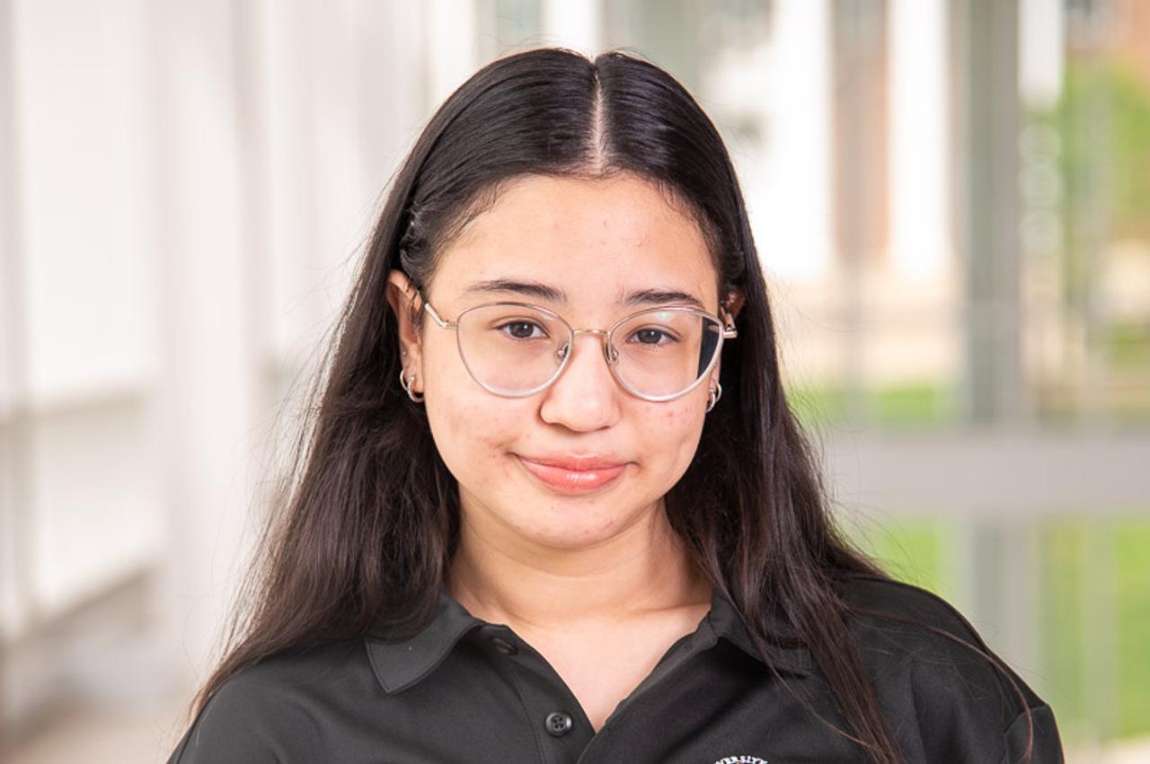 TA Yessenia in a black polo, silve glasses, and stacked silver piercings in both ears